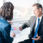 businesswoman-explaining-infographic-elements-sheet-her-male-partner 1
